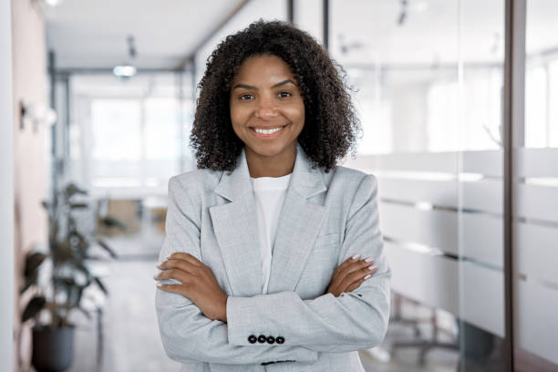 Happy smiling portrait of young African American leader manager, stand confident, crossed arms and looking at camera in business office center. Portrait of professional business woman in stylish suit.